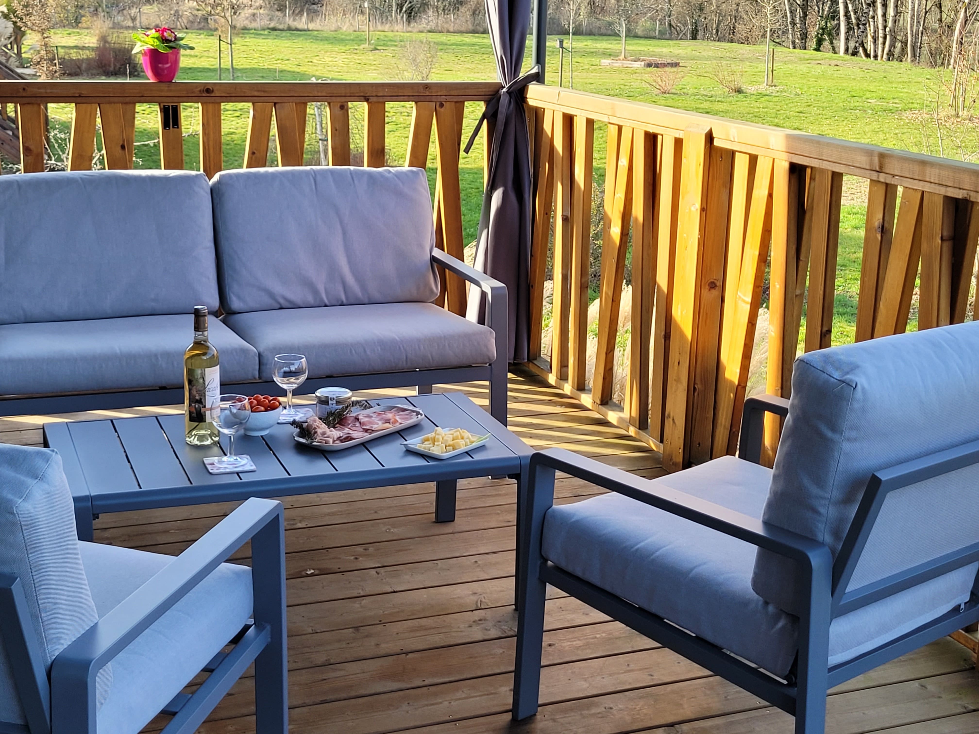Terrasse ensoleillée avec vue sur un paysage verdoyant, une table dressée pour un apéro gourmand avec des produits frais et du vin local.