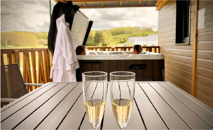 Terrasse d'un chalet en Dordogne, Brantôme avec une table, du champagne et un spa en arrière-plan.